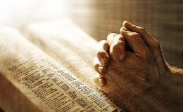 Mans hands praying on Bible